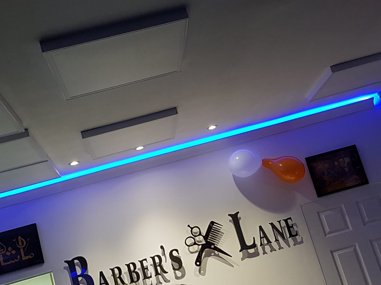Detail inside Barber's Lane: the Barber's Lane logo with crossed scissors and comb below a run of blue cove lighting