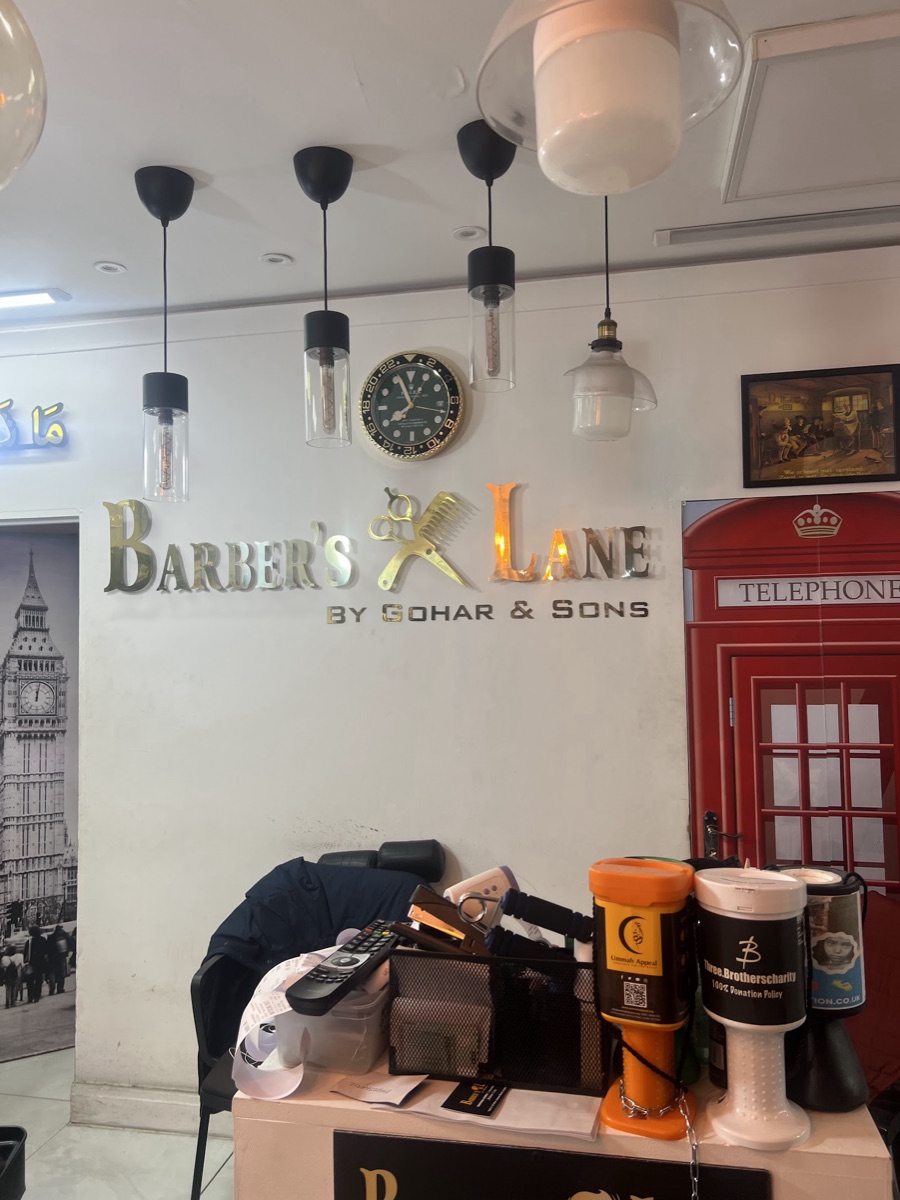 Inside Barber's Lane: brass Barber's Lane by Gohar and Sons wall lettering with crossed scissors and comb, Edison-bulb pendants and a red telephone-box feature
