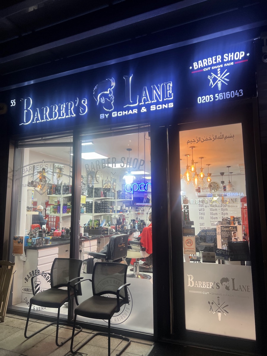 Barber's Lane shopfront lit up at night, the illuminated blue and white sign reading Barber's Lane by Gohar and Sons above the window